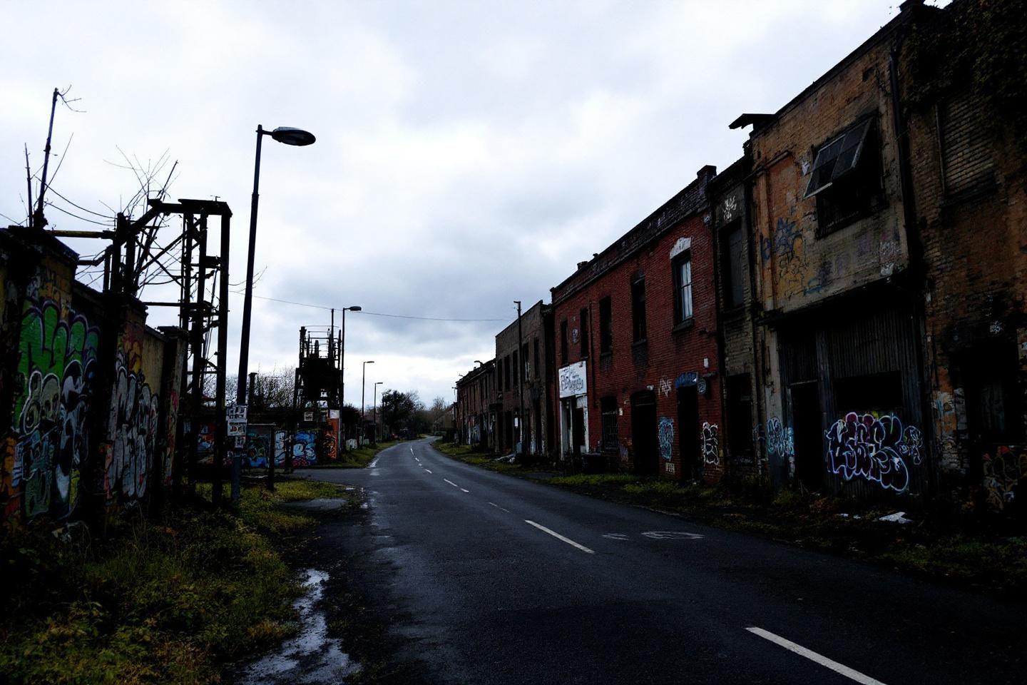 Route d&eacute;serte entre b&acirc;timents industriels tagu&eacute;s et d&eacute;cr&eacute;pits